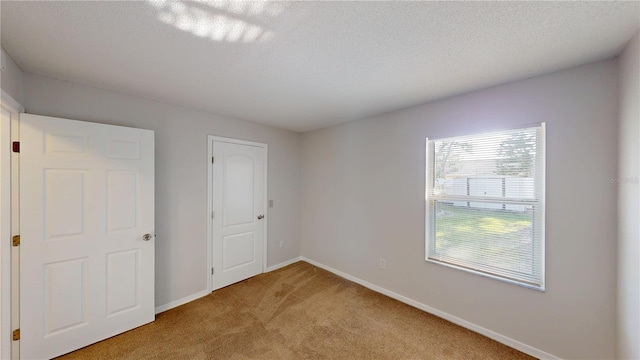 unfurnished bedroom with light colored carpet, a textured ceiling, and baseboards