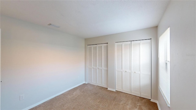 unfurnished bedroom featuring light colored carpet, visible vents, two closets, and baseboards