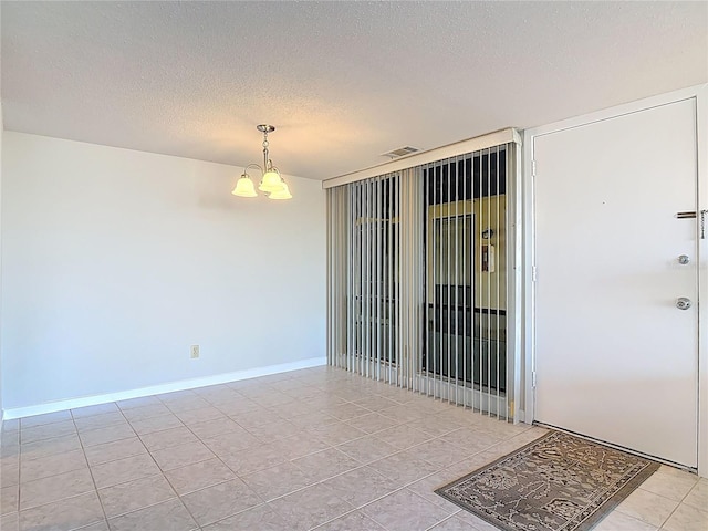 unfurnished room with baseboards, visible vents, a textured ceiling, and an inviting chandelier