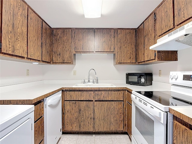 kitchen featuring under cabinet range hood, light countertops, light tile patterned floors, white appliances, and a sink