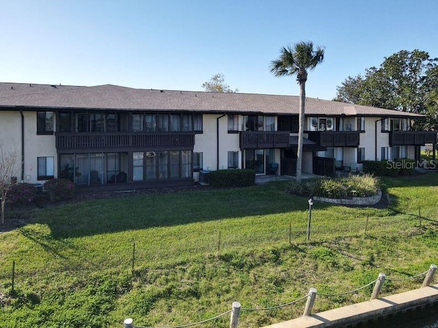 rear view of property featuring stucco siding, a lawn, and a balcony