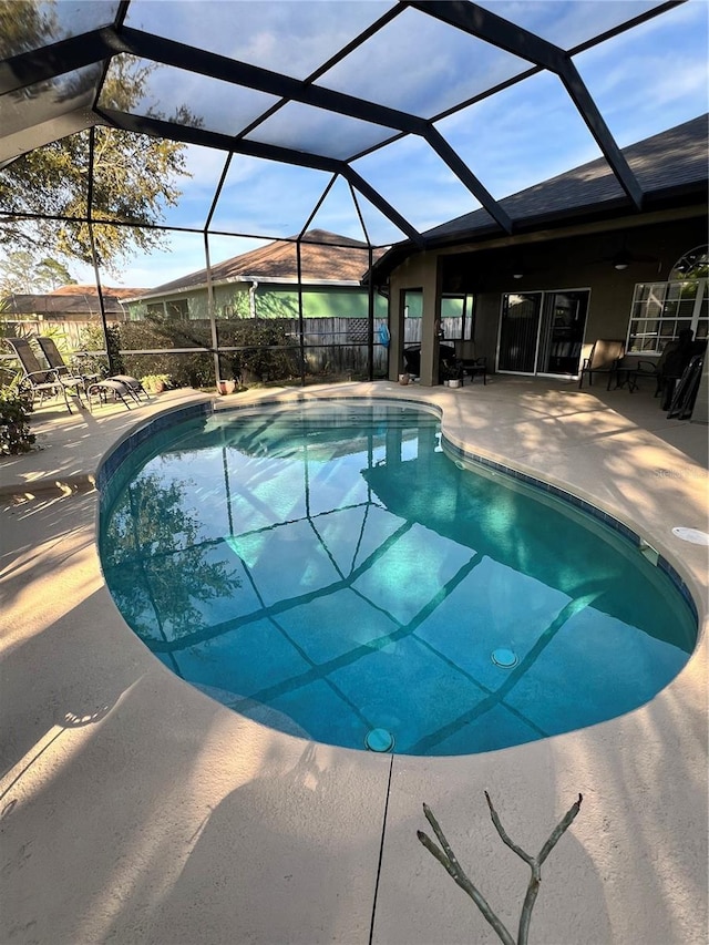 pool with a patio area, glass enclosure, and ceiling fan