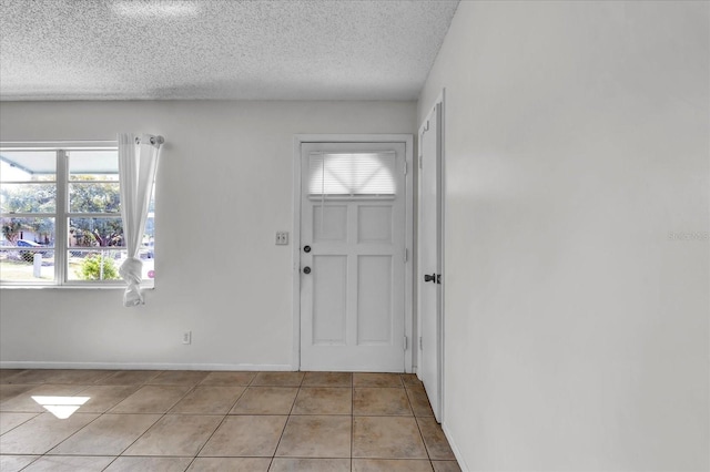 foyer entrance featuring light tile patterned floors, a textured ceiling, and baseboards