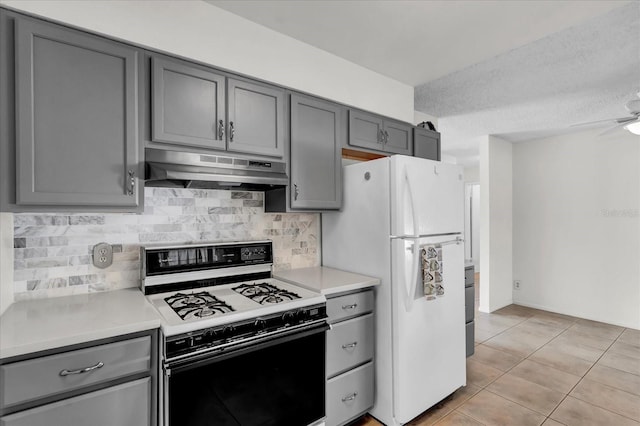 kitchen featuring freestanding refrigerator, gas range oven, under cabinet range hood, and gray cabinetry