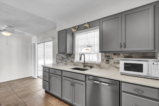 kitchen featuring gray cabinets, a sink, light countertops, white microwave, and dishwasher