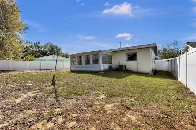 back of house with central air condition unit, a fenced backyard, a yard, a sunroom, and concrete block siding