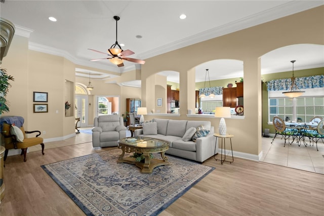 living room featuring crown molding, arched walkways, baseboards, and a ceiling fan