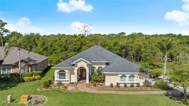 single story home featuring roof with shingles, a forest view, stucco siding, and a front yard
