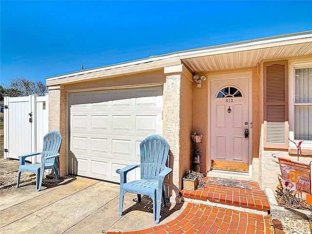 doorway to property featuring stucco siding, concrete driveway, and fence