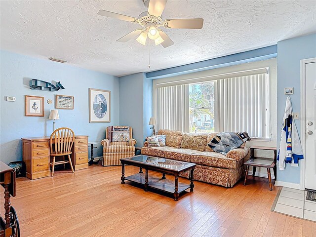 living area featuring visible vents, baseboards, light wood-style flooring, a textured ceiling, and a ceiling fan