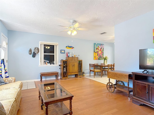 living area with a ceiling fan, light wood-type flooring, and a textured ceiling