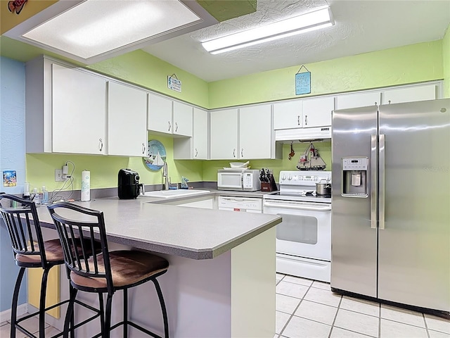 kitchen featuring white appliances, a peninsula, light tile patterned flooring, a sink, and under cabinet range hood
