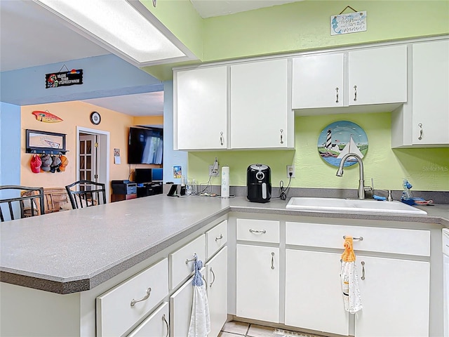 kitchen featuring white cabinetry, a peninsula, light countertops, and a sink