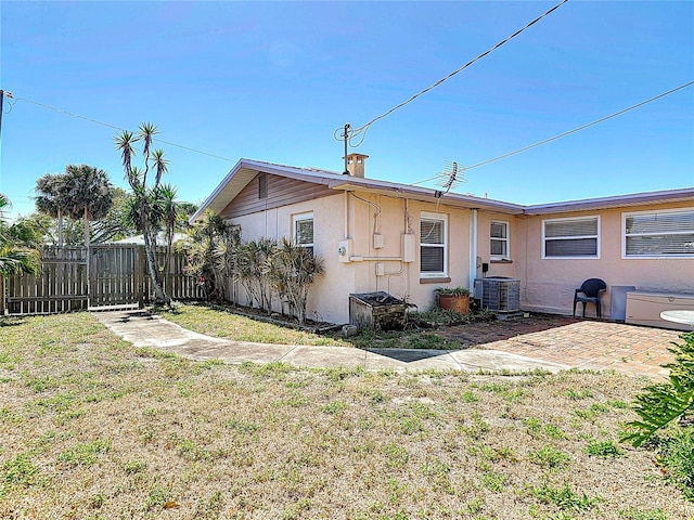 rear view of house with stucco siding, fence, a yard, central AC unit, and a patio area