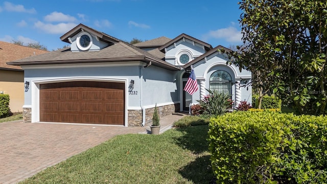 view of front facade with a front yard, driveway, an attached garage, stucco siding, and stone siding