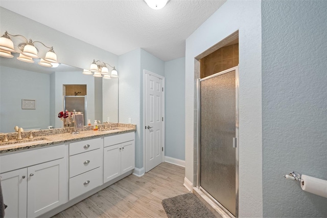 bathroom featuring double vanity, a sink, a shower stall, and wood finished floors
