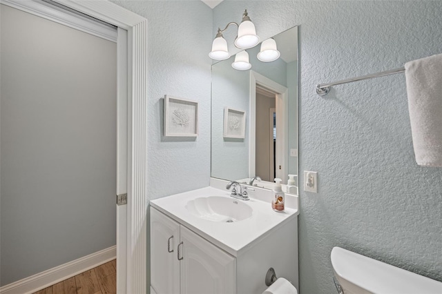 bathroom with vanity, toilet, a textured wall, a notable chandelier, and wood finished floors