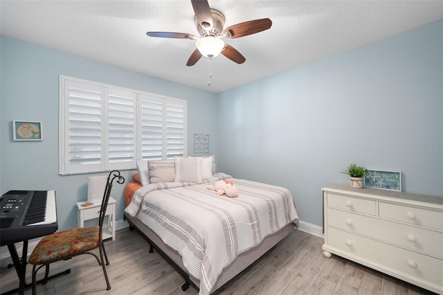 bedroom with ceiling fan, baseboards, light wood finished floors, and a textured ceiling