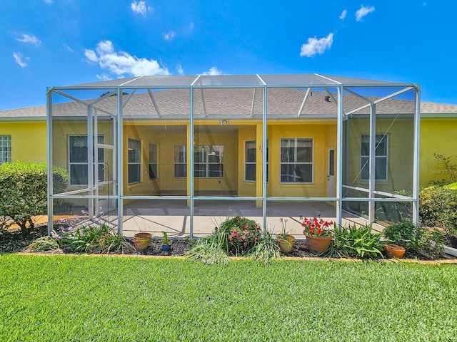 rear view of house with a patio, a lawn, roof with shingles, stucco siding, and glass enclosure