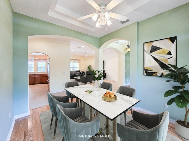 dining room featuring ceiling fan, visible vents, baseboards, arched walkways, and light wood-type flooring