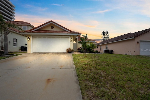 view of front facade featuring a tile roof, stucco siding, an attached garage, driveway, and a lawn