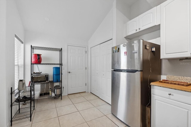 kitchen featuring freestanding refrigerator, light tile patterned floors, white cabinetry, and vaulted ceiling