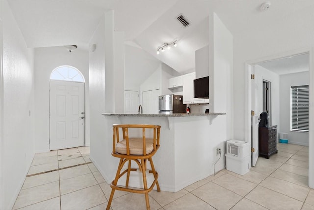 kitchen with stone counters, freestanding refrigerator, a breakfast bar area, light tile patterned floors, and visible vents