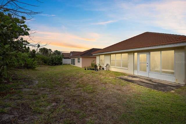 back of house with a lawn, a tile roof, and stucco siding