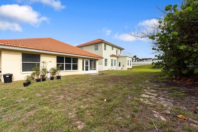 back of house with a lawn, stucco siding, and a tiled roof