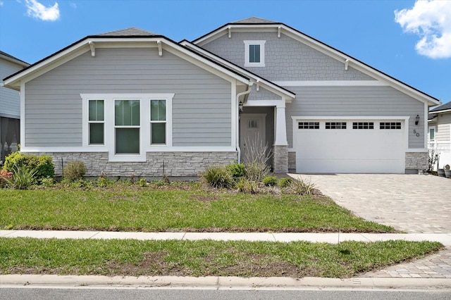 craftsman inspired home with a front yard, stone siding, decorative driveway, and an attached garage
