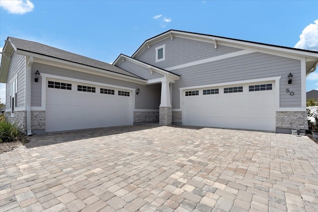 craftsman-style home with an attached garage, stone siding, and decorative driveway