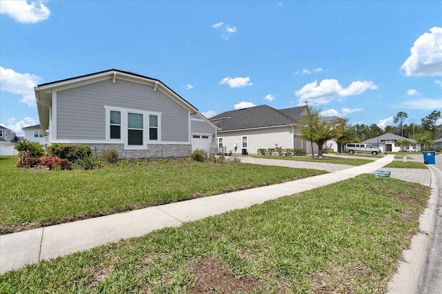 view of front of house featuring an attached garage, concrete driveway, a front yard, and stone siding
