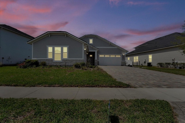 view of front of house featuring a lawn, a garage, stone siding, and decorative driveway