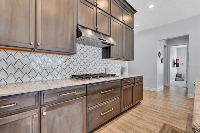 kitchen with baseboards, under cabinet range hood, decorative backsplash, light wood finished floors, and stainless steel gas stovetop