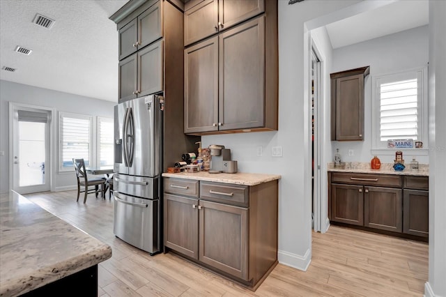 kitchen with light wood-style floors, light stone countertops, visible vents, stainless steel refrigerator with ice dispenser, and baseboards