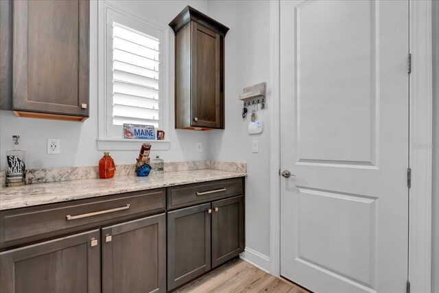 kitchen featuring light wood-style flooring, plenty of natural light, dark brown cabinetry, and light stone countertops