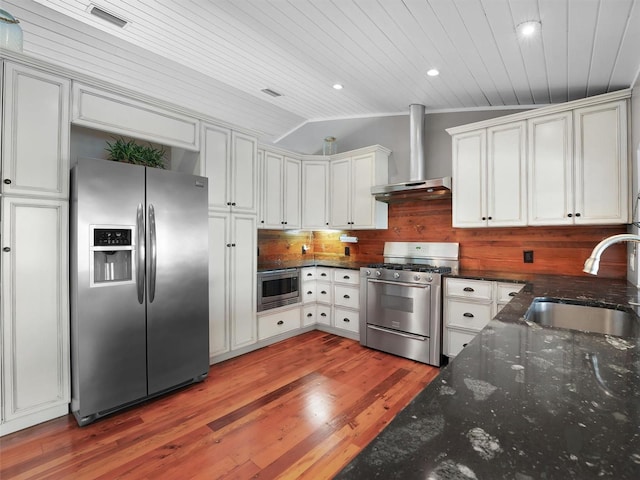 kitchen featuring lofted ceiling, wall chimney exhaust hood, a sink, light wood finished floors, and appliances with stainless steel finishes