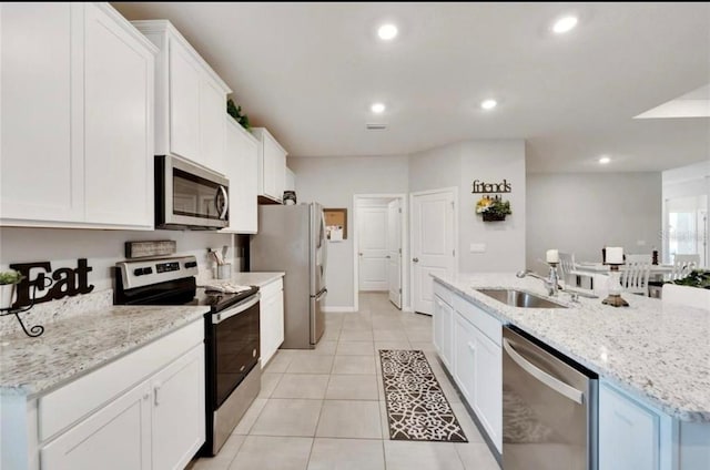 kitchen featuring an island with sink, a sink, appliances with stainless steel finishes, light tile patterned floors, and white cabinets