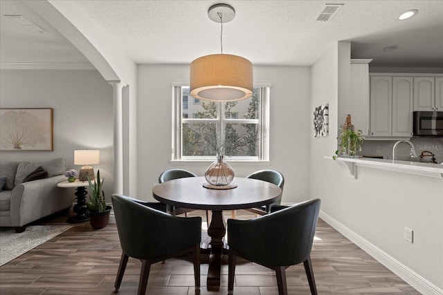 dining area with a textured ceiling, wood finished floors, baseboards, visible vents, and decorative columns