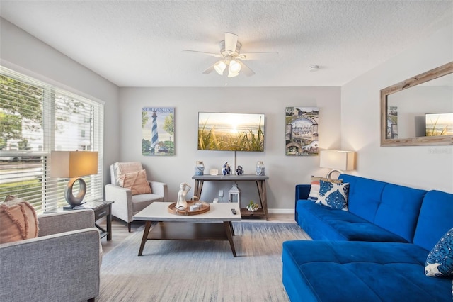 living room with a ceiling fan, a textured ceiling, baseboards, and wood finished floors
