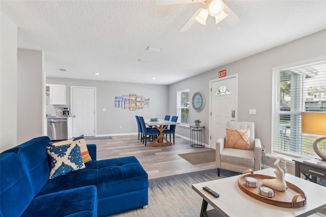 living room with a textured ceiling, light wood-style floors, baseboards, and a healthy amount of sunlight
