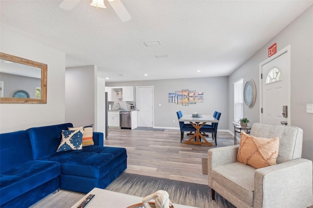 living room with a textured ceiling, baseboards, ceiling fan, recessed lighting, and light wood-style floors