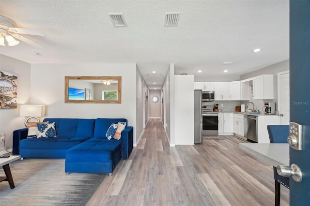 living area featuring a textured ceiling, visible vents, a ceiling fan, and light wood finished floors