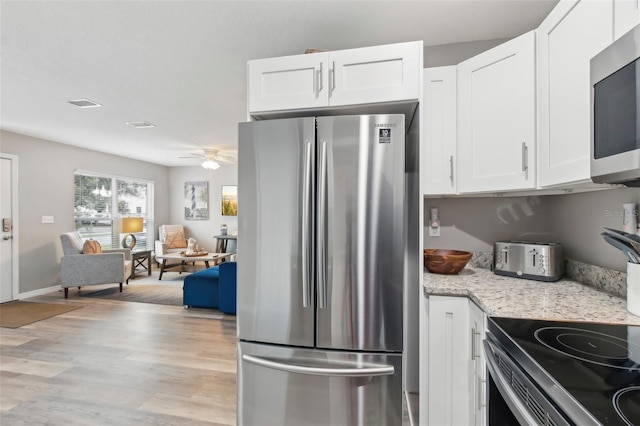 kitchen featuring white cabinets, ceiling fan, appliances with stainless steel finishes, light wood-type flooring, and light stone counters
