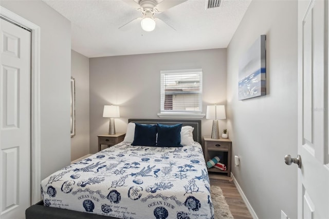 bedroom featuring a ceiling fan, wood finished floors, a textured ceiling, baseboards, and visible vents