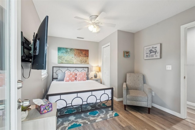 bedroom with a ceiling fan, visible vents, baseboards, and wood finished floors
