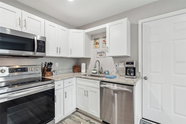 kitchen featuring white cabinetry, light wood-type flooring, a sink, light stone counters, and appliances with stainless steel finishes