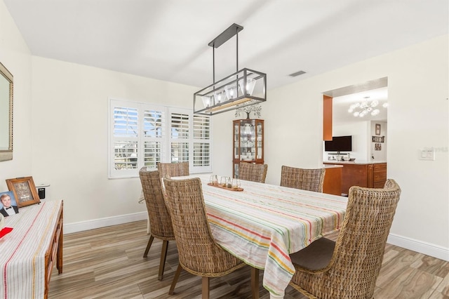 dining area featuring baseboards, a notable chandelier, visible vents, and light wood-style flooring