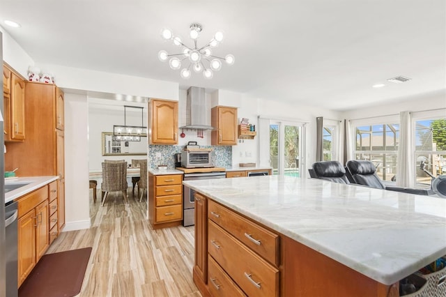 kitchen featuring wall chimney range hood, plenty of natural light, stainless steel appliances, and a chandelier