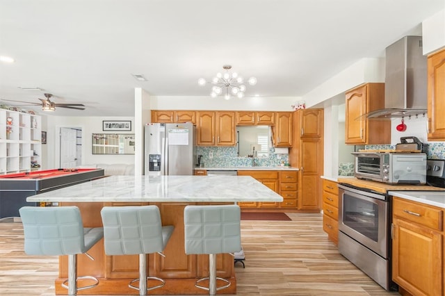 kitchen featuring stainless steel appliances, a center island, a toaster, backsplash, and wall chimney exhaust hood